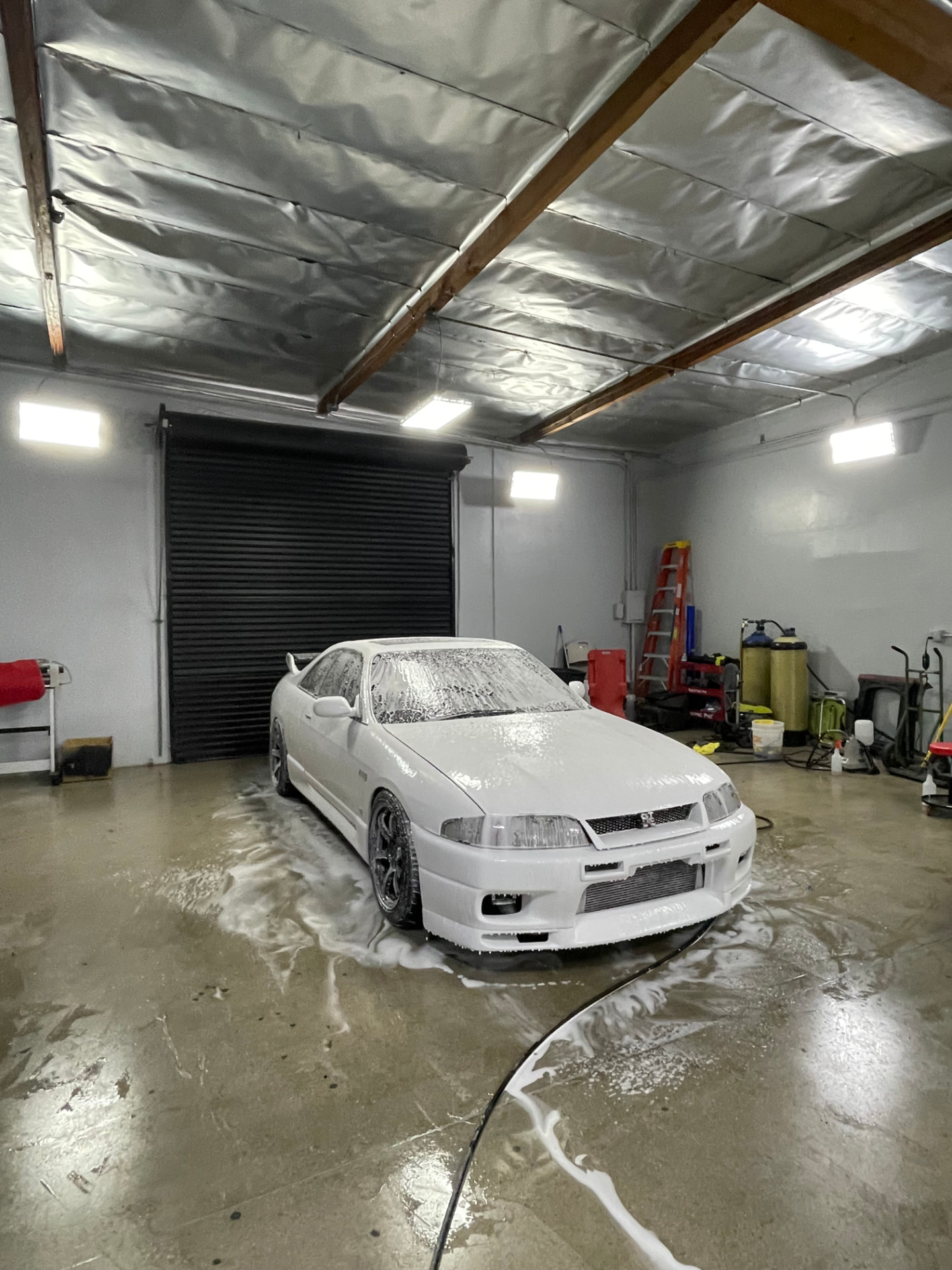 White Nissan Skyline covered in snow foam during a wash